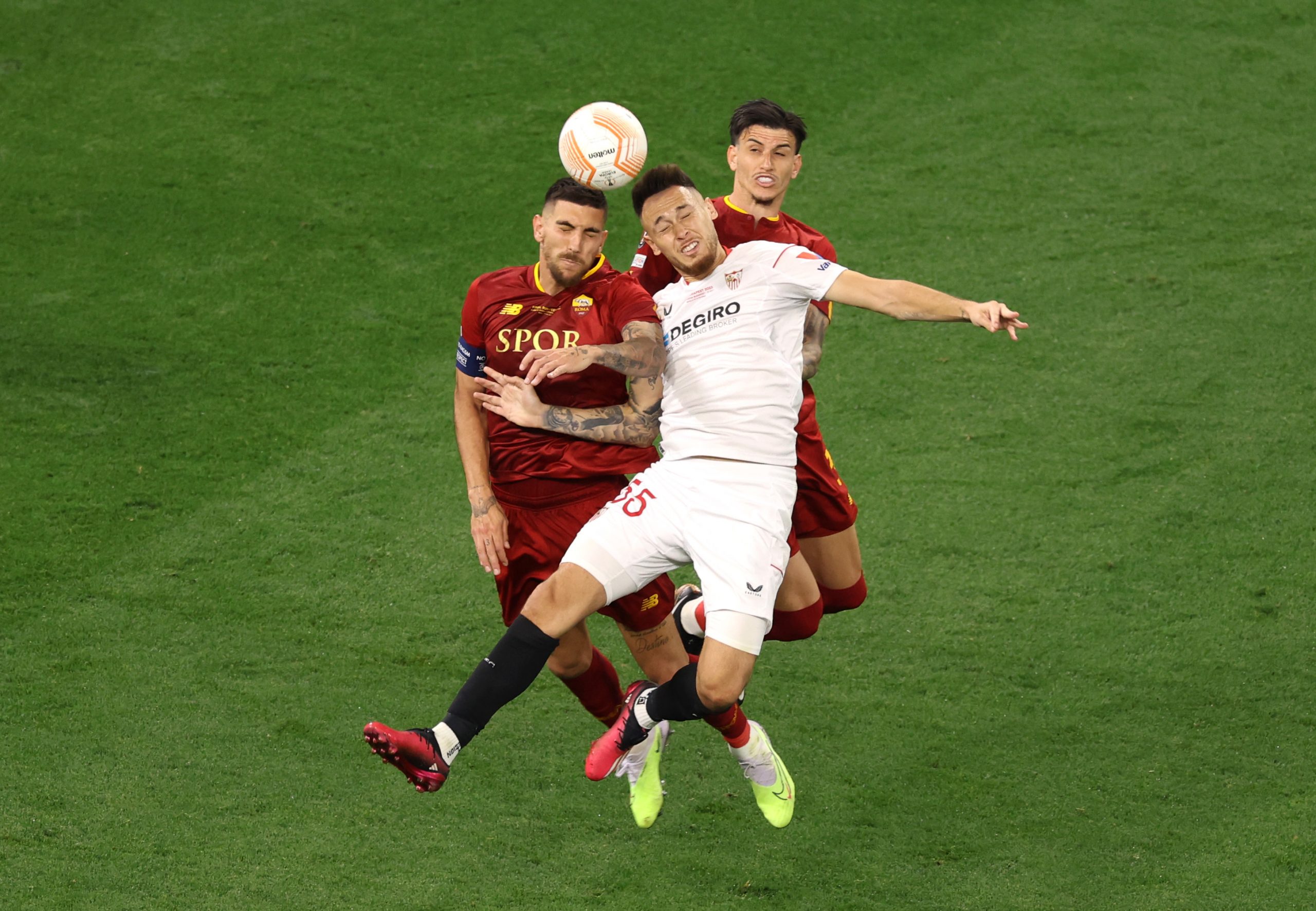 Lucas Ocampos of Sevilla FC battles for a header with Lorenzo Pellegrini and Roger Ibanez of AS Roma.